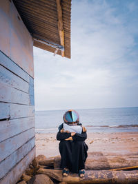 Full length of woman wearing helmet sitting against sea