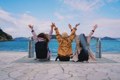 Rear view of friends sitting by sea against sky