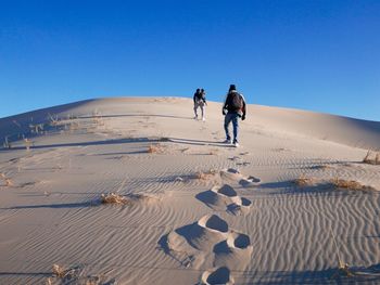 People walking on sand at beach against clear blue sky