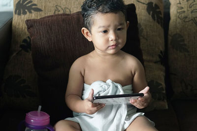 Full length of baby boy using mobile phone while sitting on sofa at home