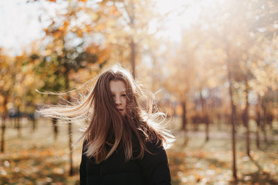 Young teenage girl with flowing hair standing  against sunny lights walking in autumn park. 