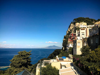 High angle view of cityscape by sea against clear blue sky