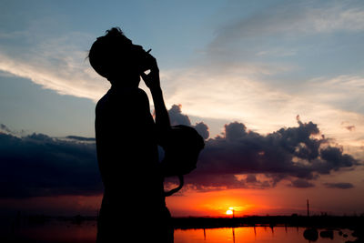 Silhouette man smoking cigarette against sky during sunset