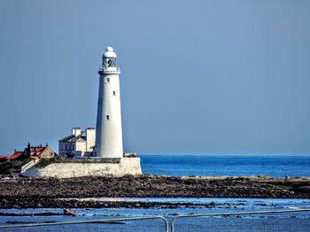 Lighthouse by sea against sky