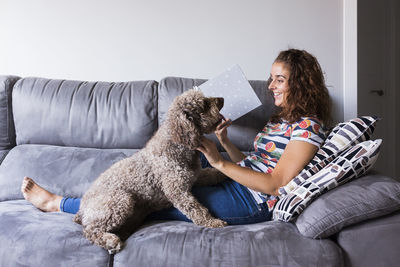 Smiling woman with dog sitting on sofa at home