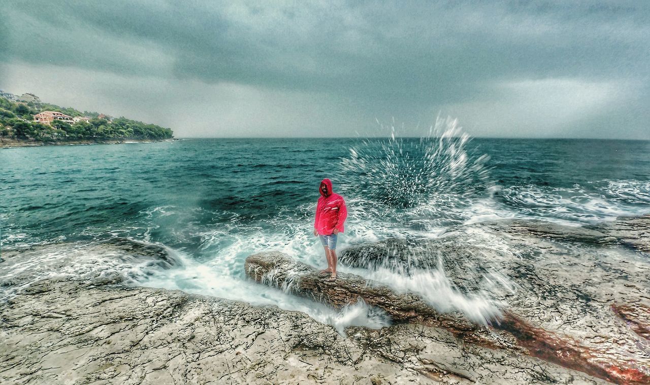 REAR VIEW OF WOMAN STANDING IN SEA AGAINST SKY