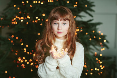 Happy young girl sitting by the christmas tree with garland