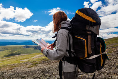 Stylish woman with backpack hiking, orient themselves to the terrain, study map and navigate 