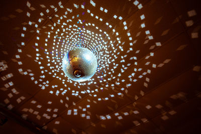 Low angle view of illuminated disco ball hanging from ceiling in nightclub