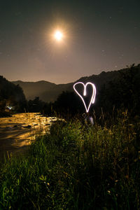 Heart shape light painting over grassy field by river at night