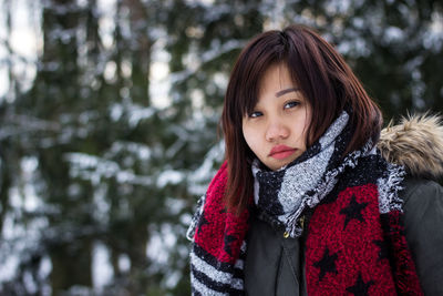 Portrait of young woman in warm clothing standing against trees during winter