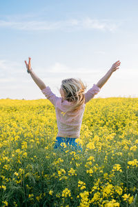 Rear view of woman with arms raised standing at field against cloudy sky