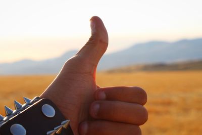 Close-up of human hand against sky during sunset