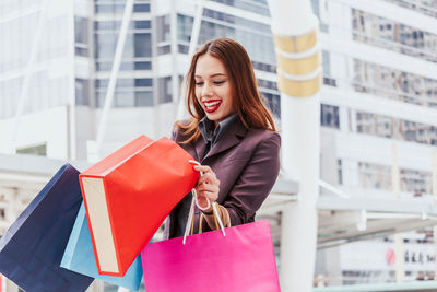 Portrait of happy young woman with shopping bags standing on walkway 