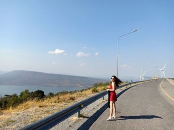 Portrait of woman standing by railing on road against sky