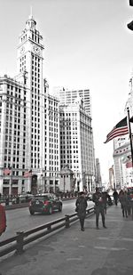 People on street by modern buildings in city against sky