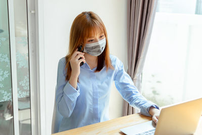 Portrait of young woman using phone while standing on table