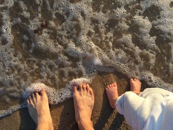 Low section of father and daughter standing on wet shore