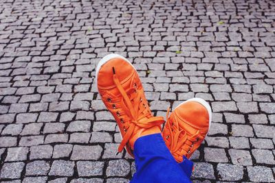 Low section of woman wearing orange shoes on cobbled footpath