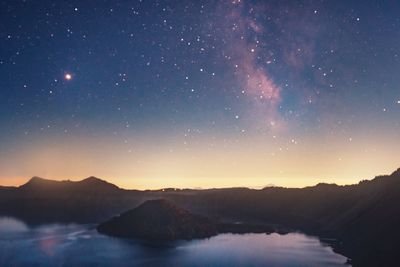 Scenic view of lake and mountains against sky at night