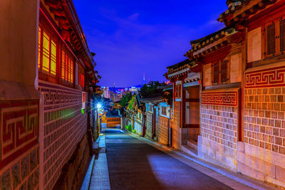 Illuminated street amidst buildings against sky at night