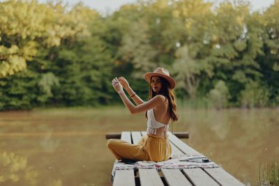 Side view of woman sitting on pier over lake