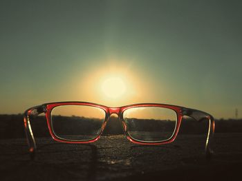 Close-up of sunglasses against sky during sunset