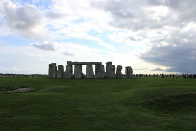 Tourists opposite to stonehenge field against cloudy sky