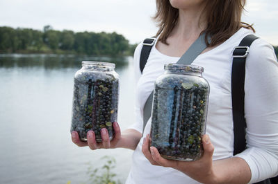 Midsection of woman holding blueberries in jars at lakeshore