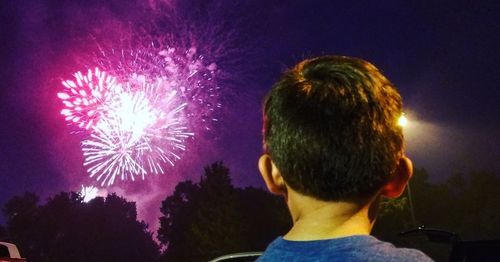 Rear view of man with fireworks against sky at night