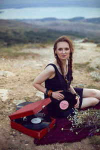 Young woman sit in nature in a black dress next to an old gramophone and listens to music