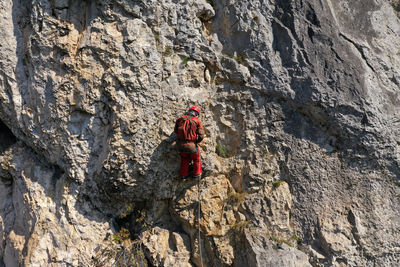 Flying near a mountain rescuer rappelling on a rocky wall with a drone