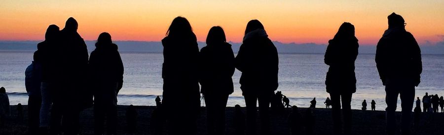 Panoramic view of silhouette people standing at beach during sunset
