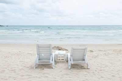 Chairs at beach against cloudy sky