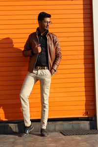 Young man looking away while standing against orange wall