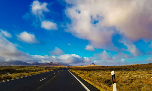 Empty road along volcanic landscape against cloudy sky