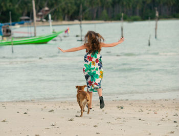 Rear view of woman running with dog at beach at ko samui
