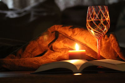 Close-up of illuminated candle and book in darkroom