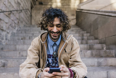 Cheerful man using mobile phone while sitting on steps