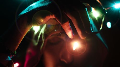 Cropped hand of young man holding illuminated string lights in darkroom
