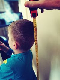 Cropped hand holding tape measure against boy at home