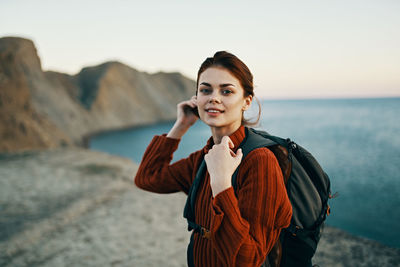 Portrait of young woman standing at beach against sky