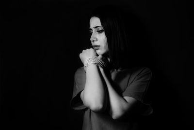 Woman hands tied with string against black background