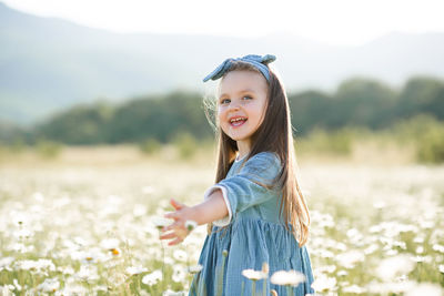 Smiling cute baby girl 3-4 year old wear stylish dress with flowers in bloom camomile meadow outdoor