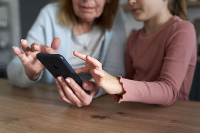 Midsection of grandmother and granddaughter talking on video call at home