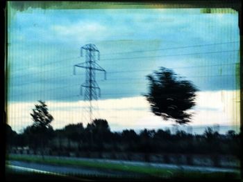 Electricity pylon on field against cloudy sky