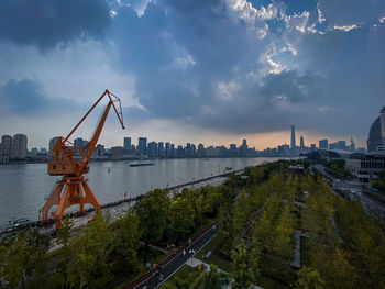 Cranes by river against sky in city