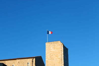 Low angle view of flag against building against clear blue sky