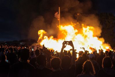 Crowd looking at bonfire against sky during night