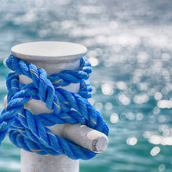 Close-up of blue rope tied on bollard by sea